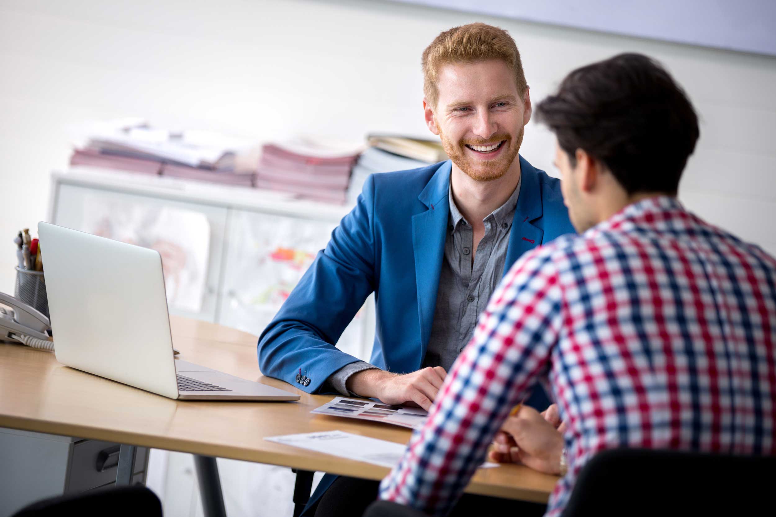 Zwei junge Ingenieure sitzen lachend an einem Tisch mit Computer