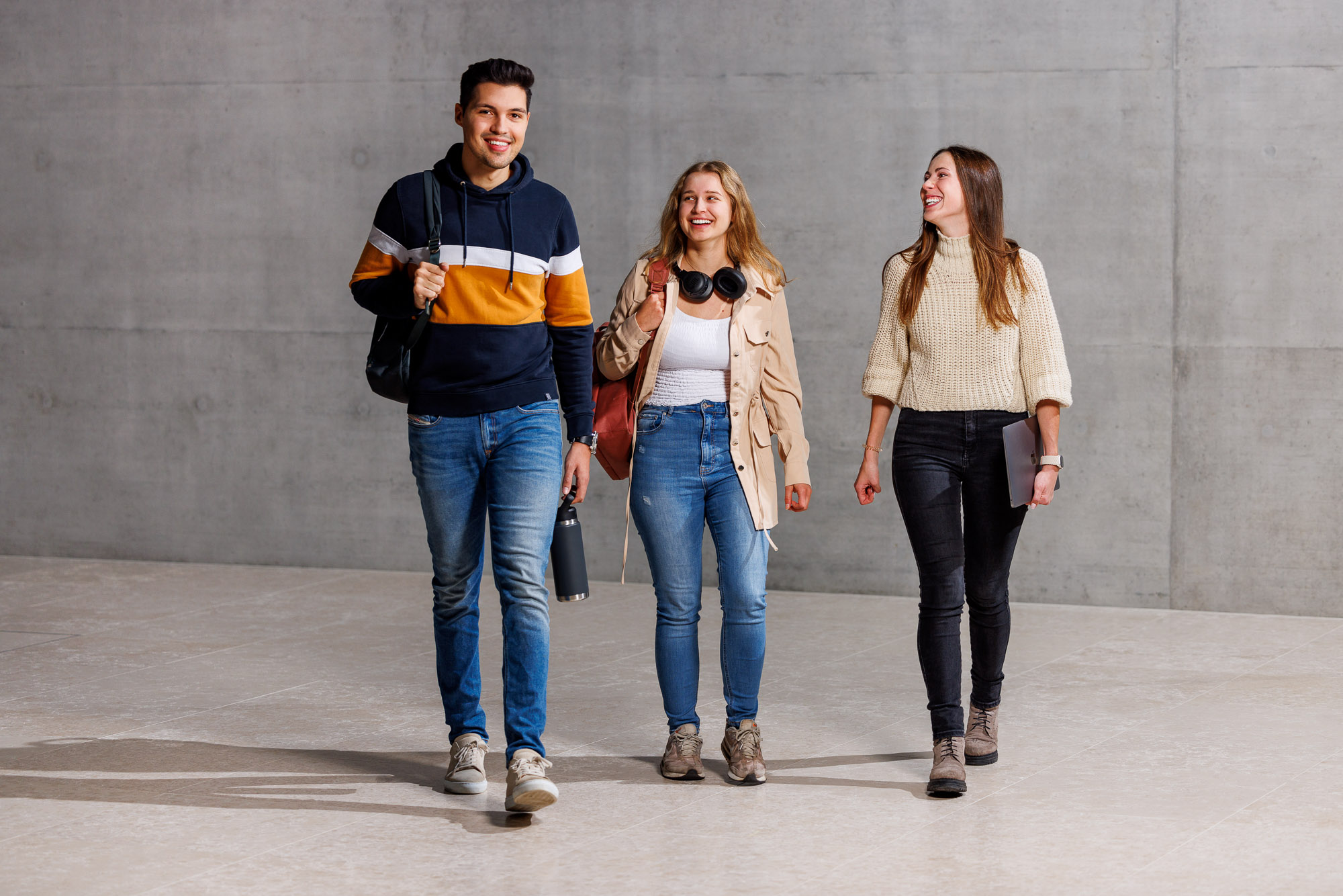 Zwei Frauen und ein Mann laufen vor einer grauen Wand.