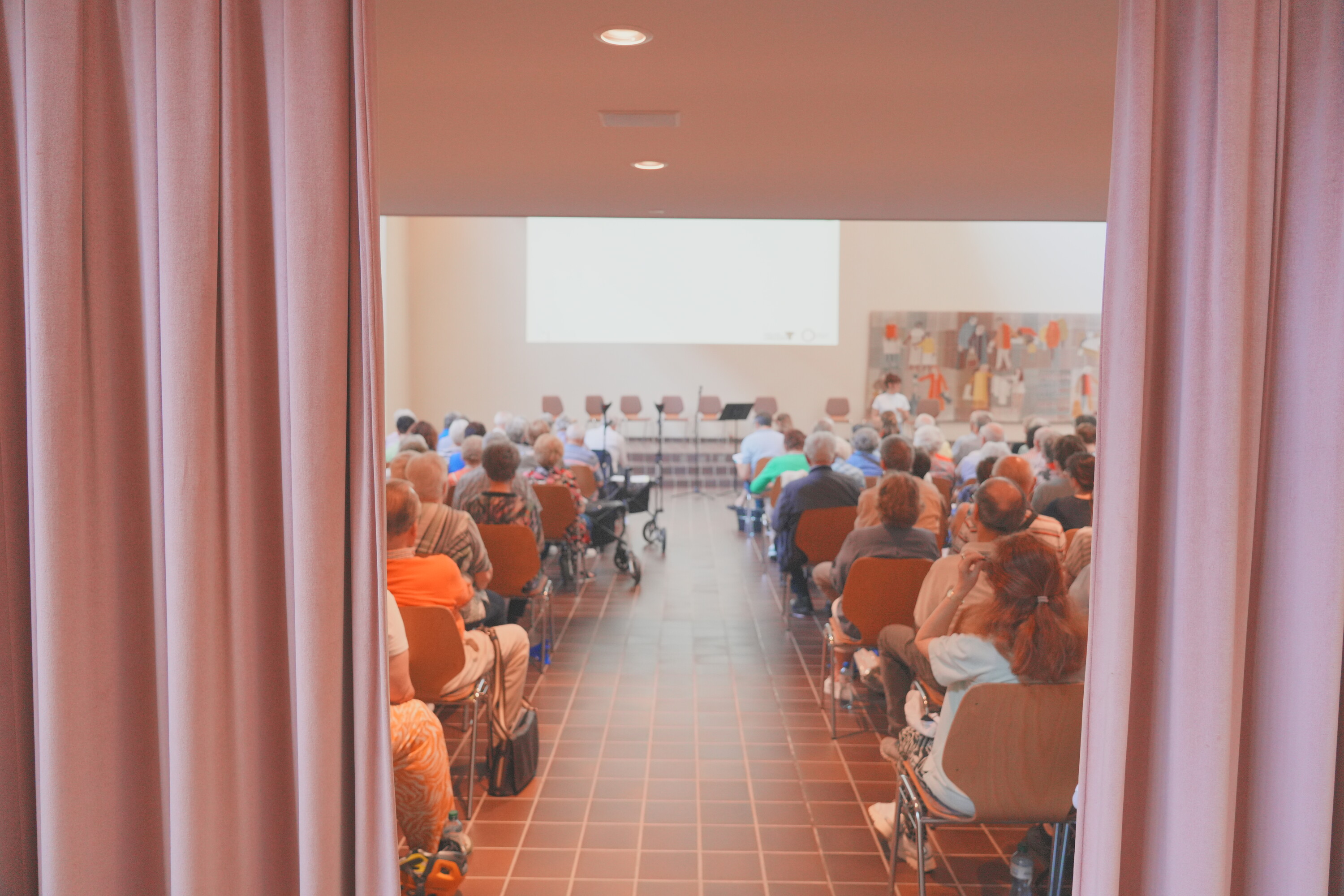 Blick zwischen Vorhang mit Menschen im Vortragssaal